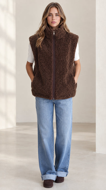 Front view of woman wearing brown sherpa fleece zip-up vest with jeans