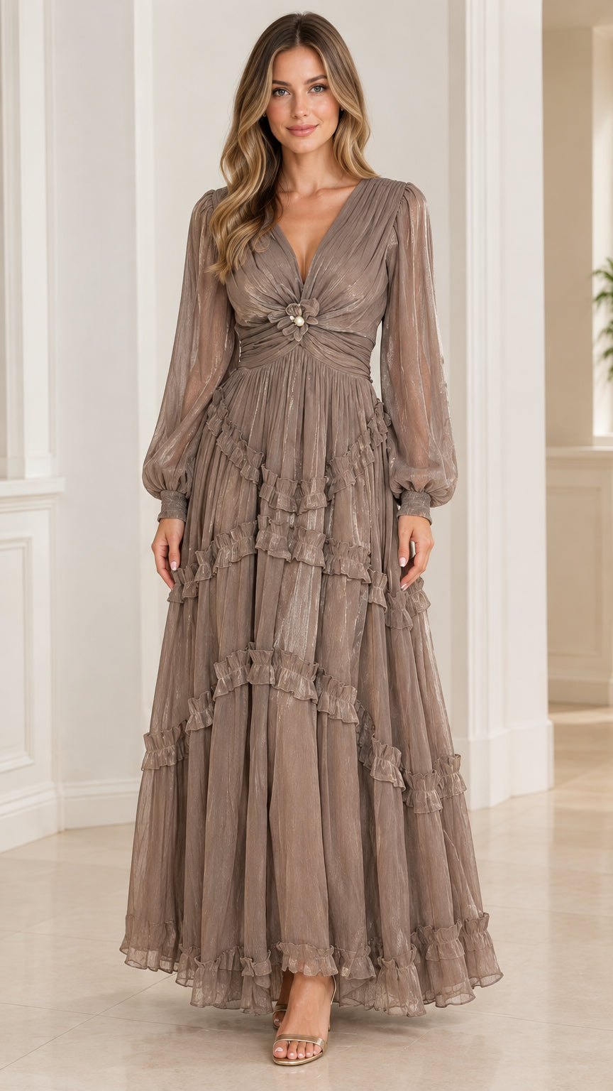 Front view of model wearing taupe plissé tiered maxi dress with long bishop sleeves and pearl brooch