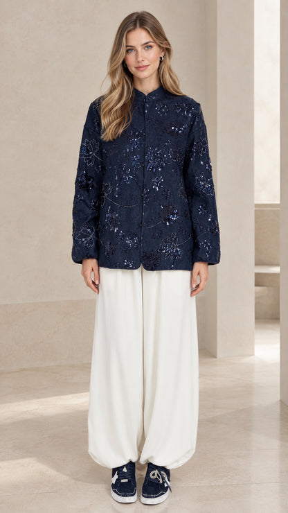Front full view of woman wearing navy blue floral sequin embroidered button-down jacket with white wide-leg trousers