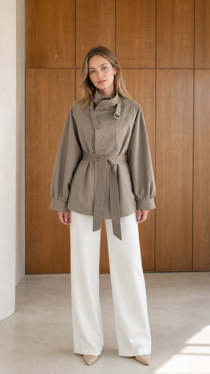 Front view of model wearing taupe high neck belted short trench jacket with white wide leg trousers