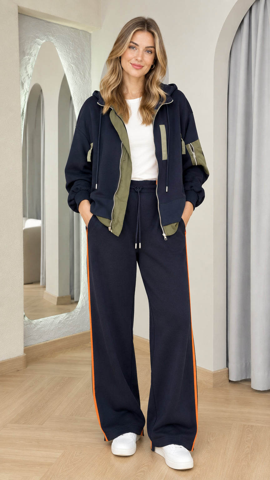 Front view of woman wearing navy zip-up hoodie and matching wide-leg track pants set with orange side stripe