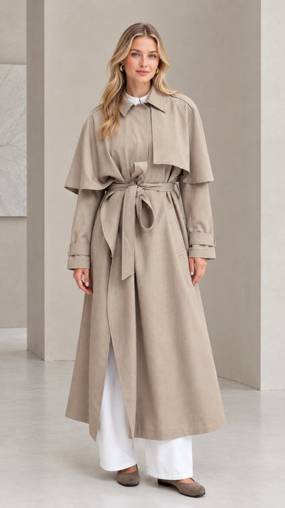 Front full view of women's taupe capelet maxi trench coat with tie belt