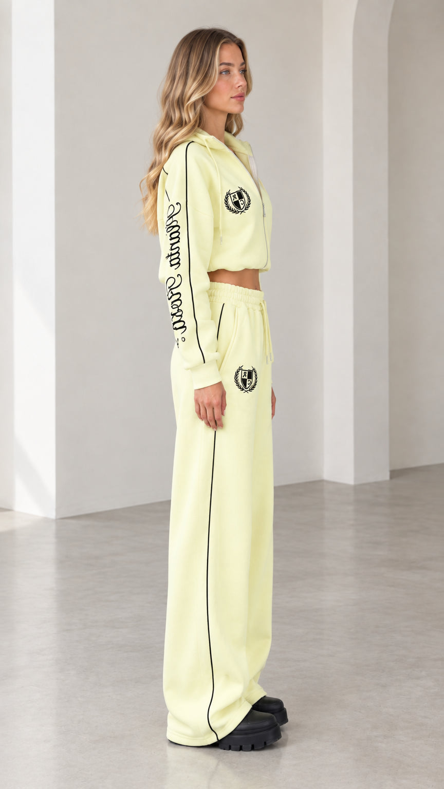 Side profile view of model in butter yellow tracksuit set showing sleeve embroidery and piping