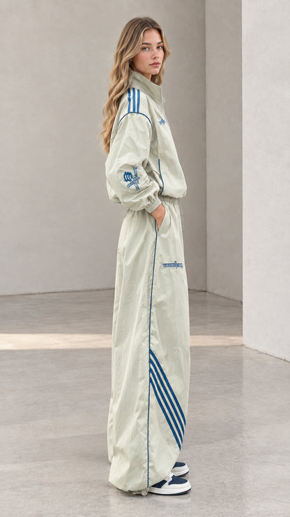 Side view of woman posing in sage green wide-leg tracksuit with blue side stripes