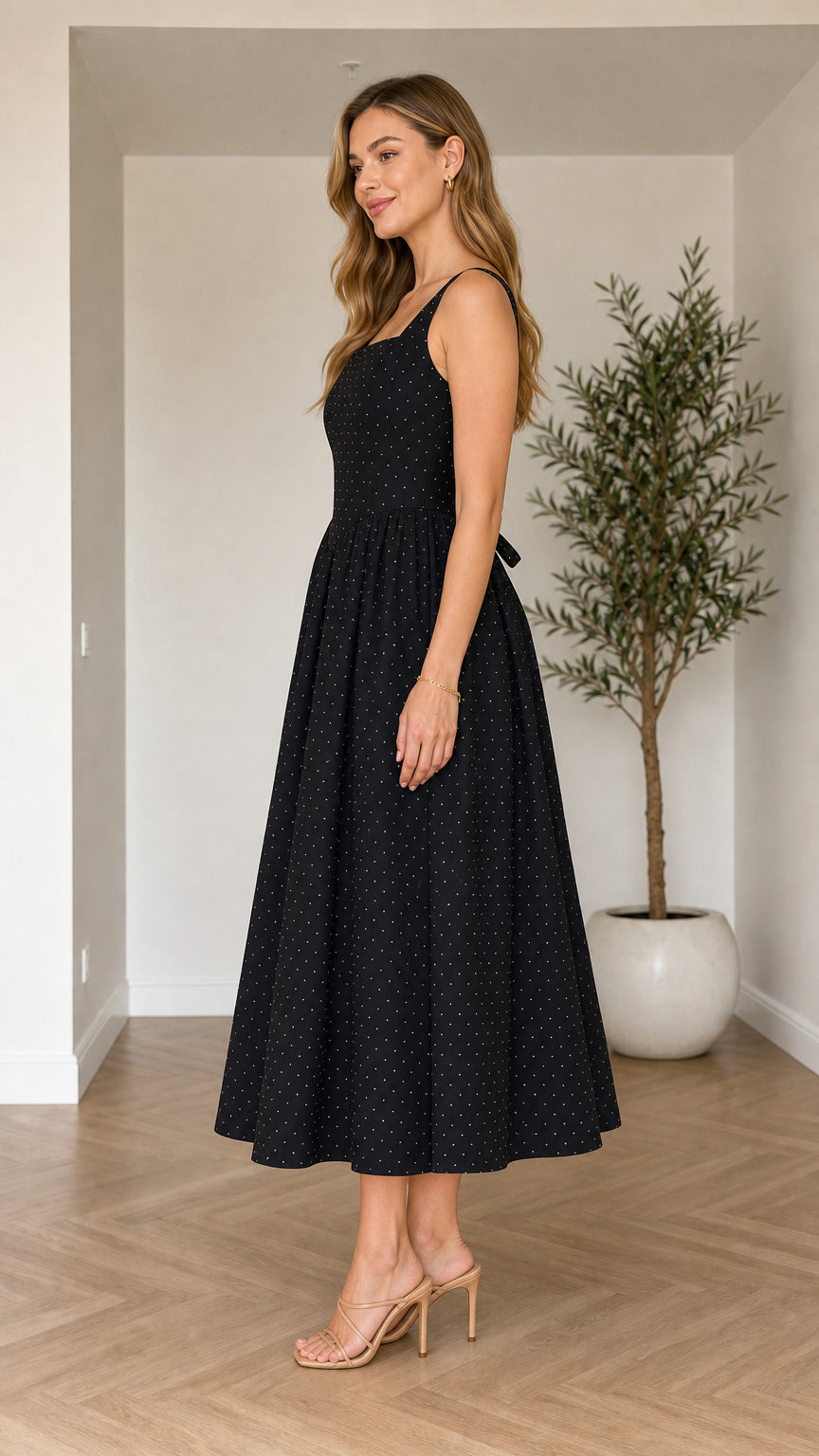 Side profile view of model wearing black polka dot sleeveless pleated dress
