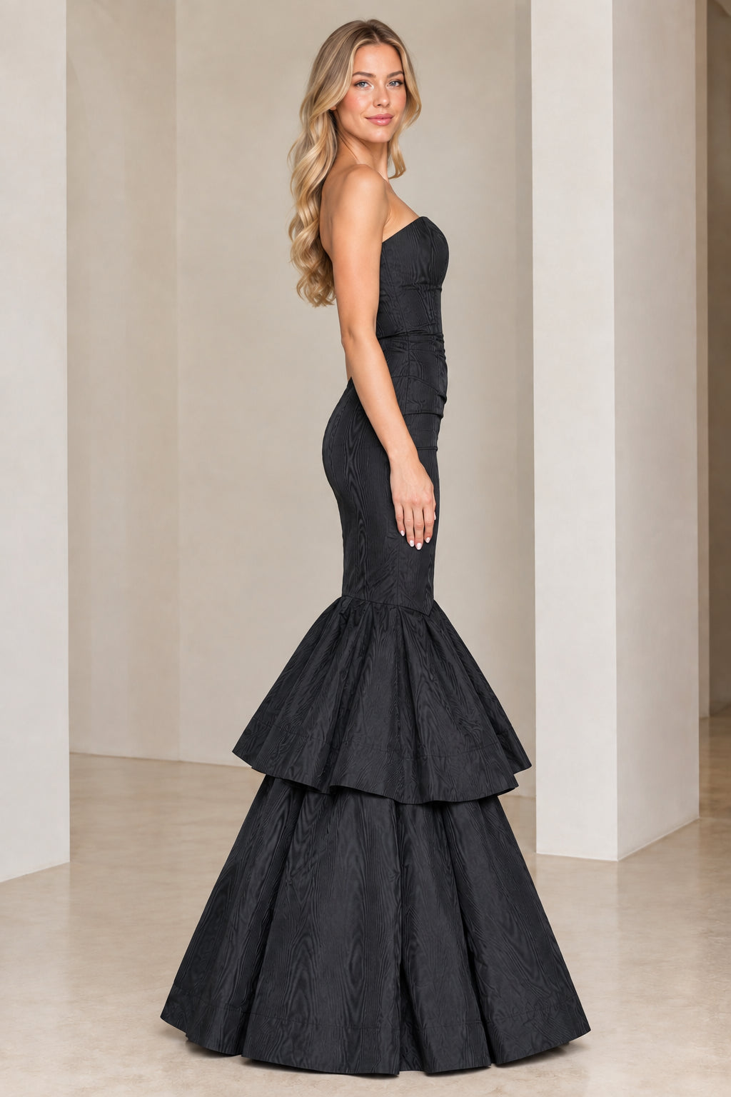 Side profile of black strapless mermaid maxi dress with flared tiers
