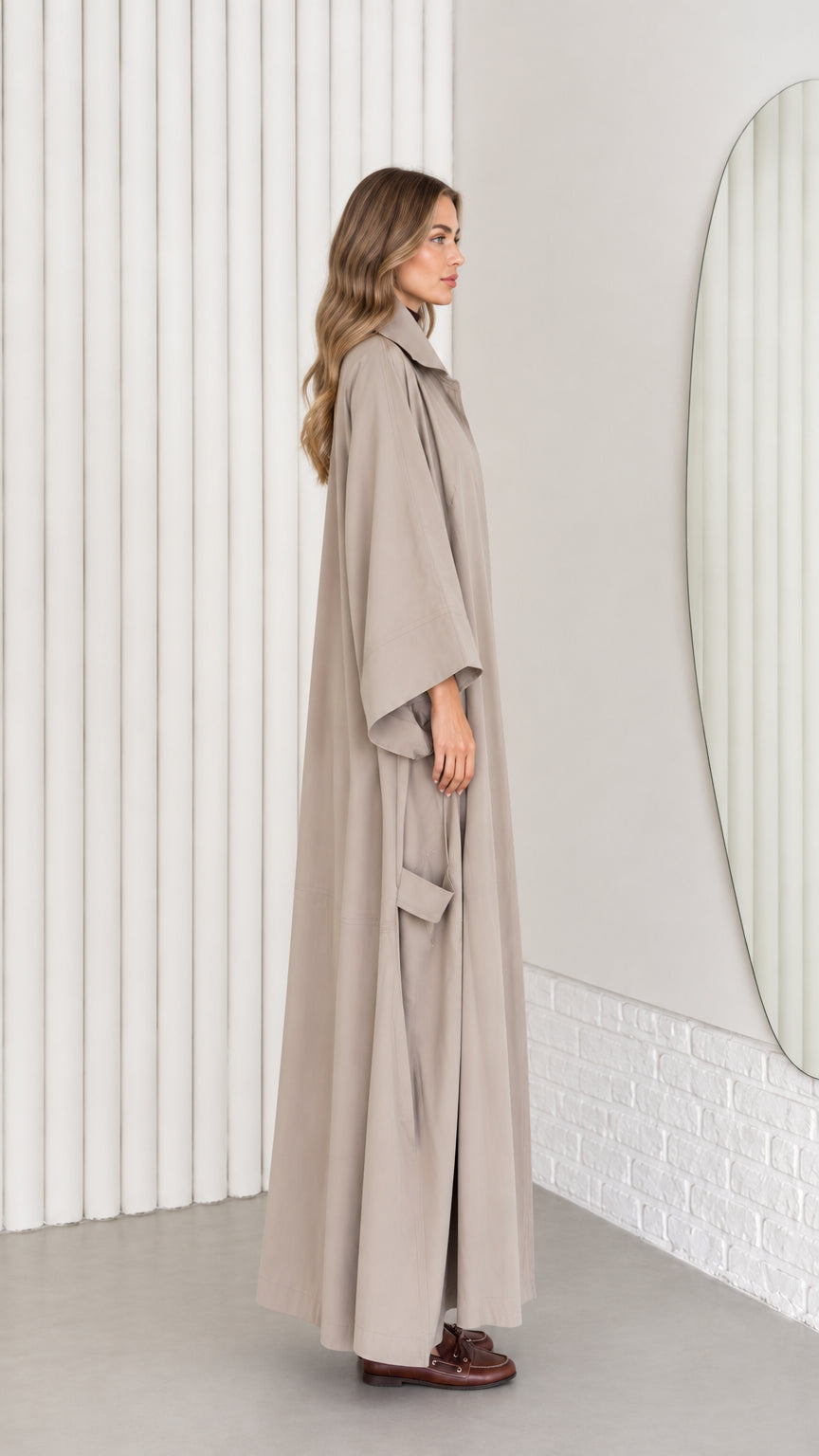 Side profile view of taupe maxi trench coat showing fluid floor-length drape