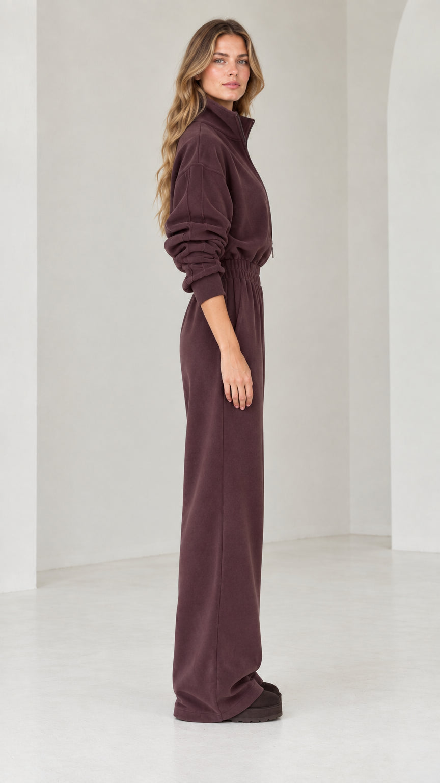 Side view of model wearing chocolate brown half-zip wide leg fleece jumpsuit