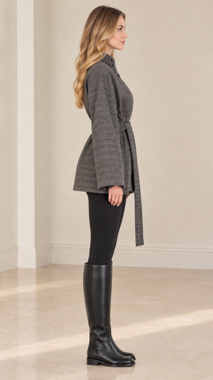 Side profile of woman wearing grey plaid belted jacket with knee-high black boots