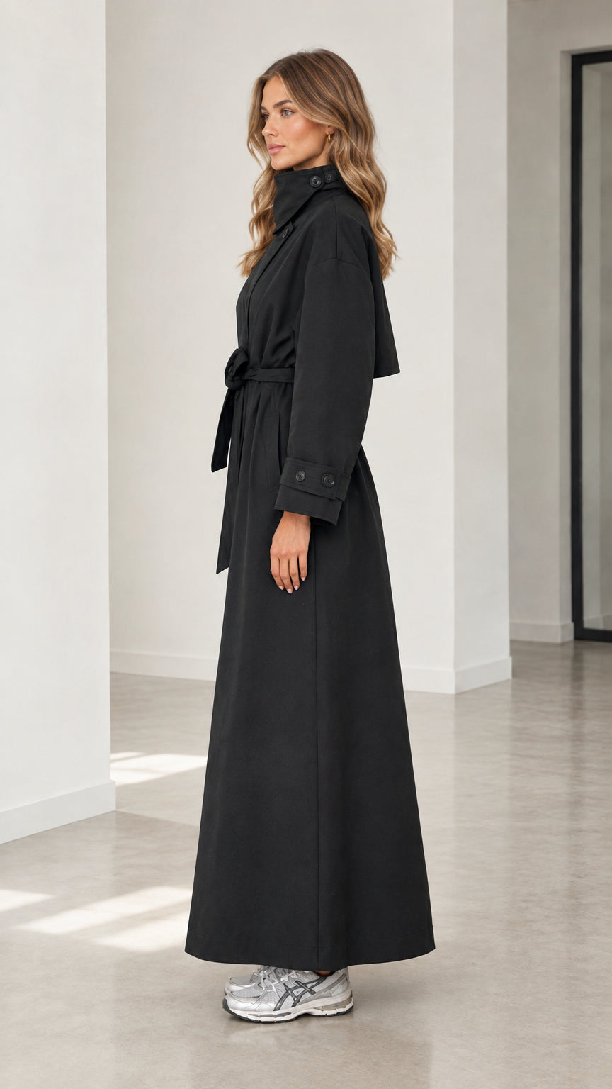 Side profile view of woman wearing long black belted trench coat with funnel collar