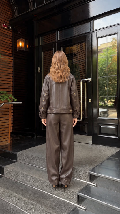 Back full view of woman in dark brown faux leather snap jacket and pants