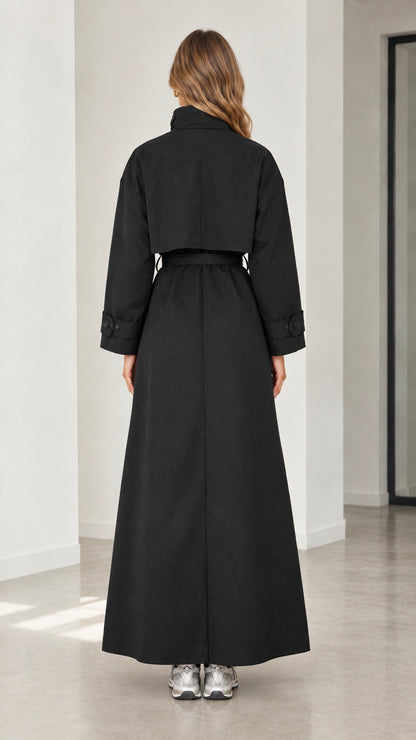 Back view of woman wearing full-length black trench coat with back storm flap detail