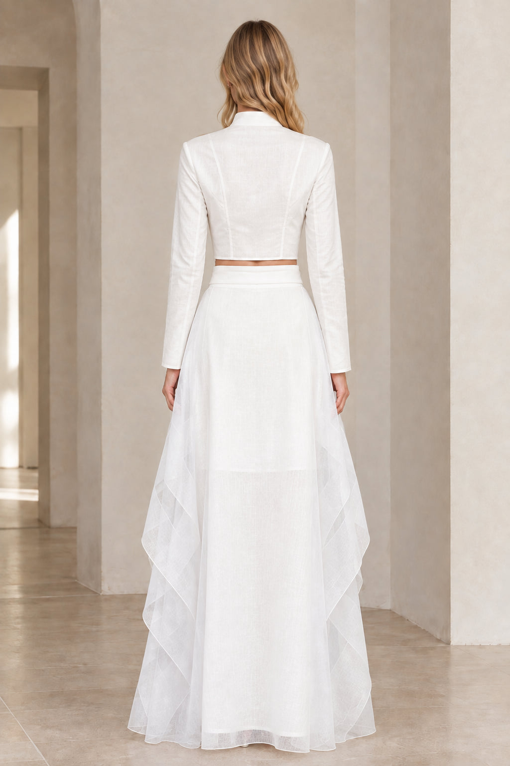 Back view of model wearing white long-sleeve crop top and flowy maxi skirt