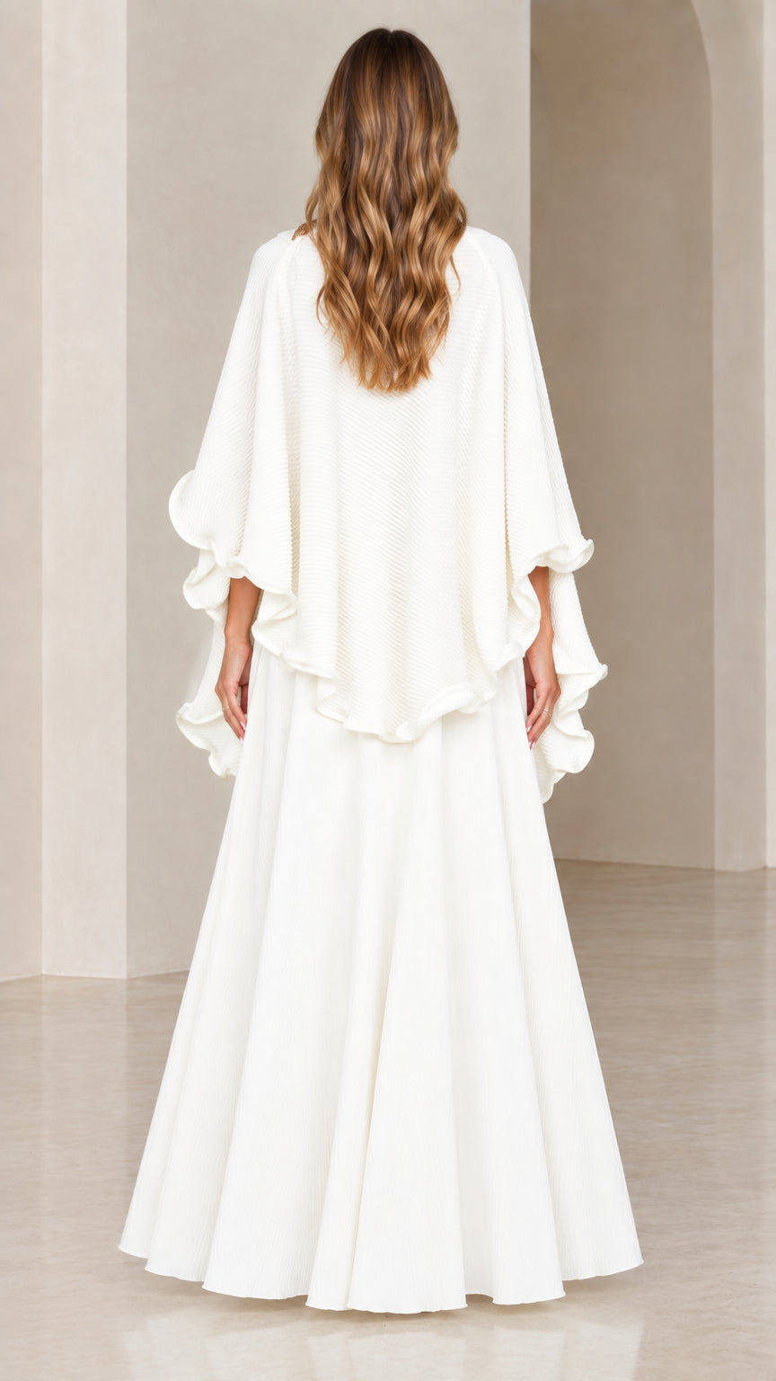 Back view of model wearing white textured capelet top and sweeping skirt