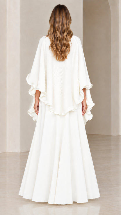 Back view of model wearing white textured capelet top and sweeping skirt