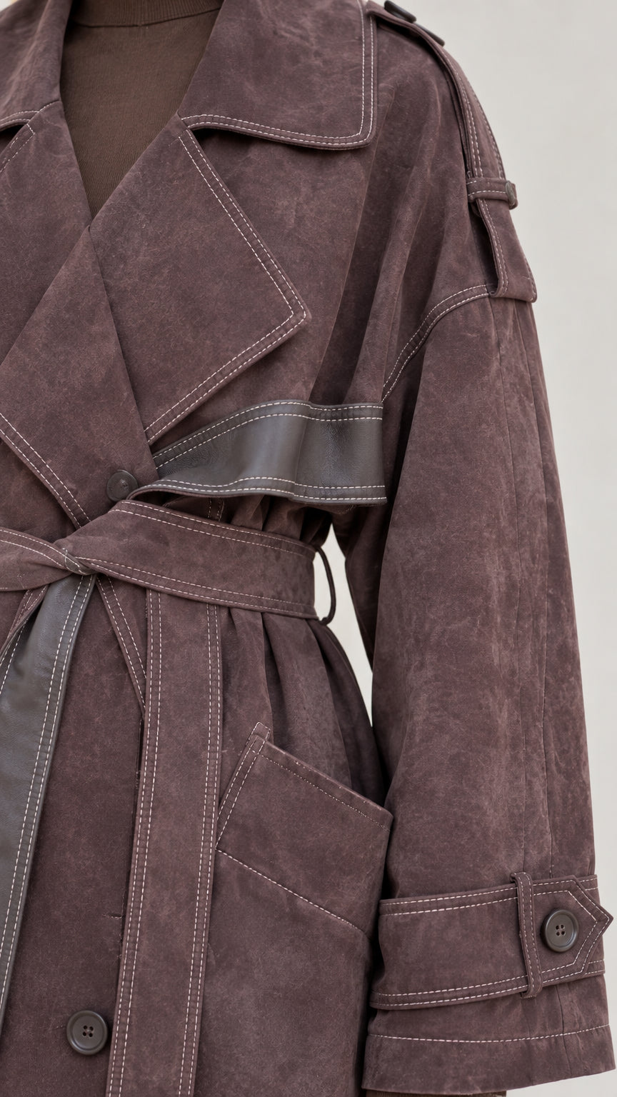 Close-up detail of contrast topstitching, wide lapel, and cuff strap on brown coat