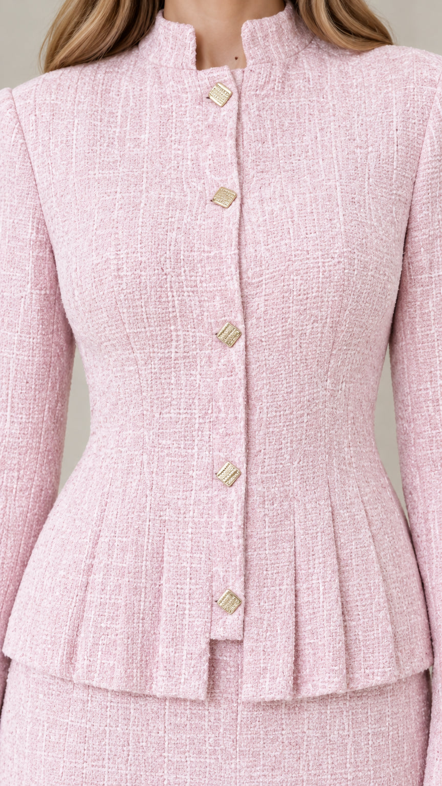 Close-up detail of blush pink textured tweed fabric, metallic buttons, and peplum pleats