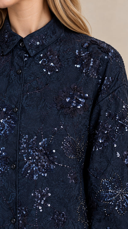 Close-up detail of navy blue textured fabric showing intricate floral embroidery and shimmering sequin accents