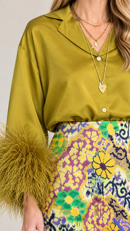 Close-up of olive green satin shirt collar, gold jewelry, and feather cuff detail