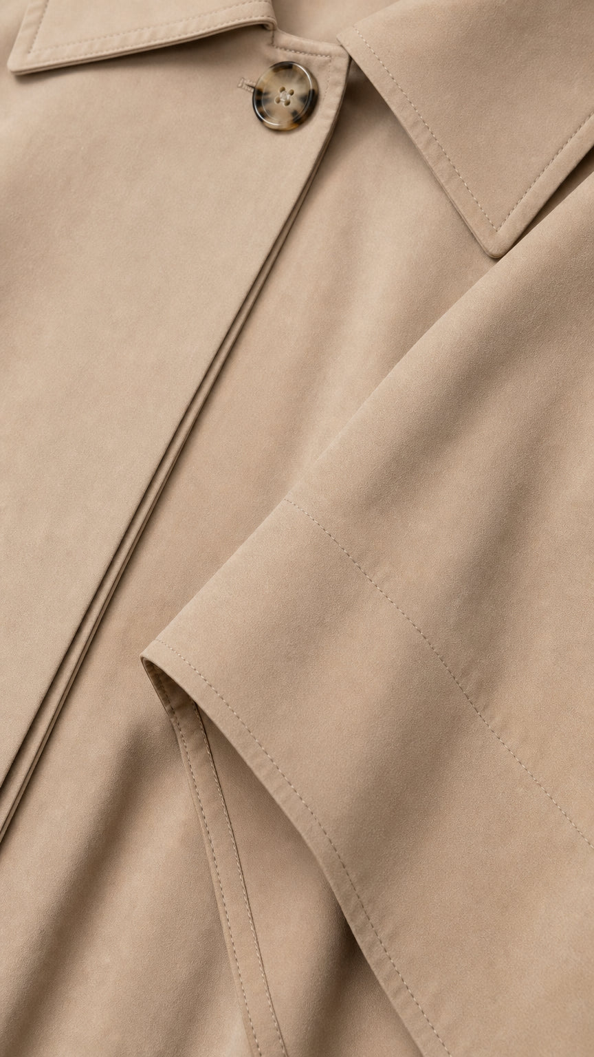 Close-up detail of beige cape collar, tortoiseshell button, and neat seam stitching