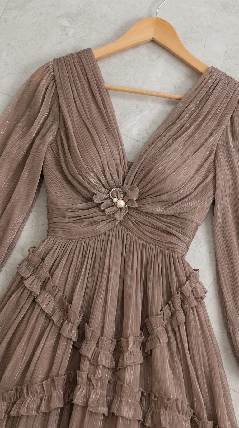 Close-up detail of taupe dress on wooden hanger showing pleated V-neckline and flower pearl brooch