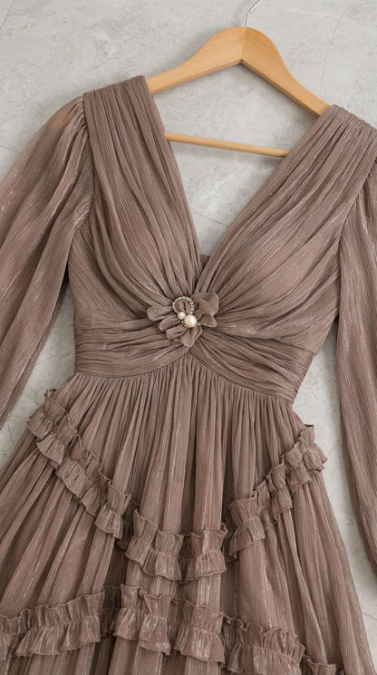 Close-up detail of taupe dress on wooden hanger showing pleated V-neckline and flower pearl brooch