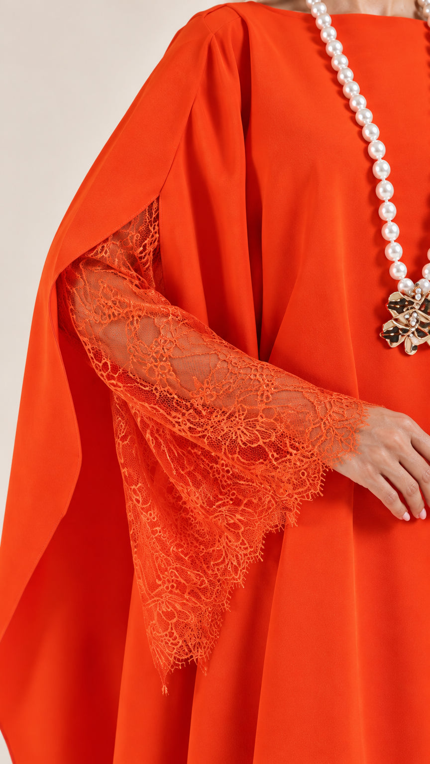 Close-up detail of orange dress showing delicate floral lace sleeve and cape drape