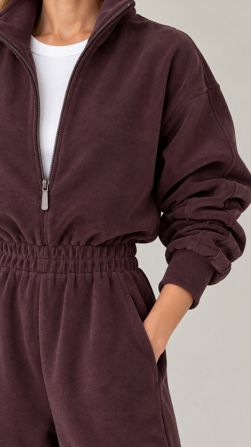 Close-up detail of half-zip neckline and smocked waist on chocolate fleece jumpsuit