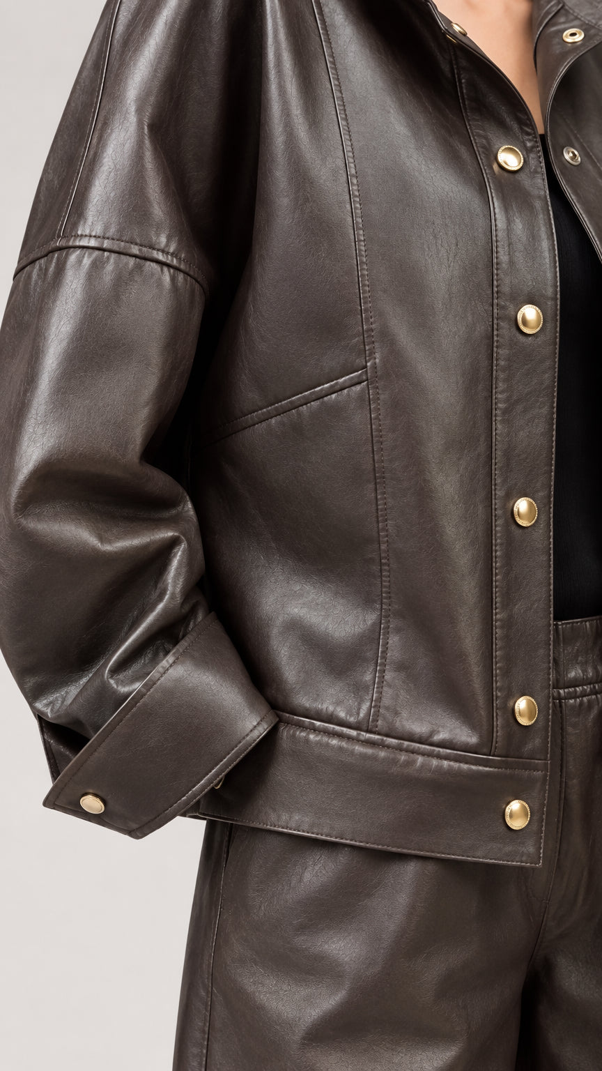 Close-up detail of dark brown faux leather jacket with snap buttons and tailored seam lines