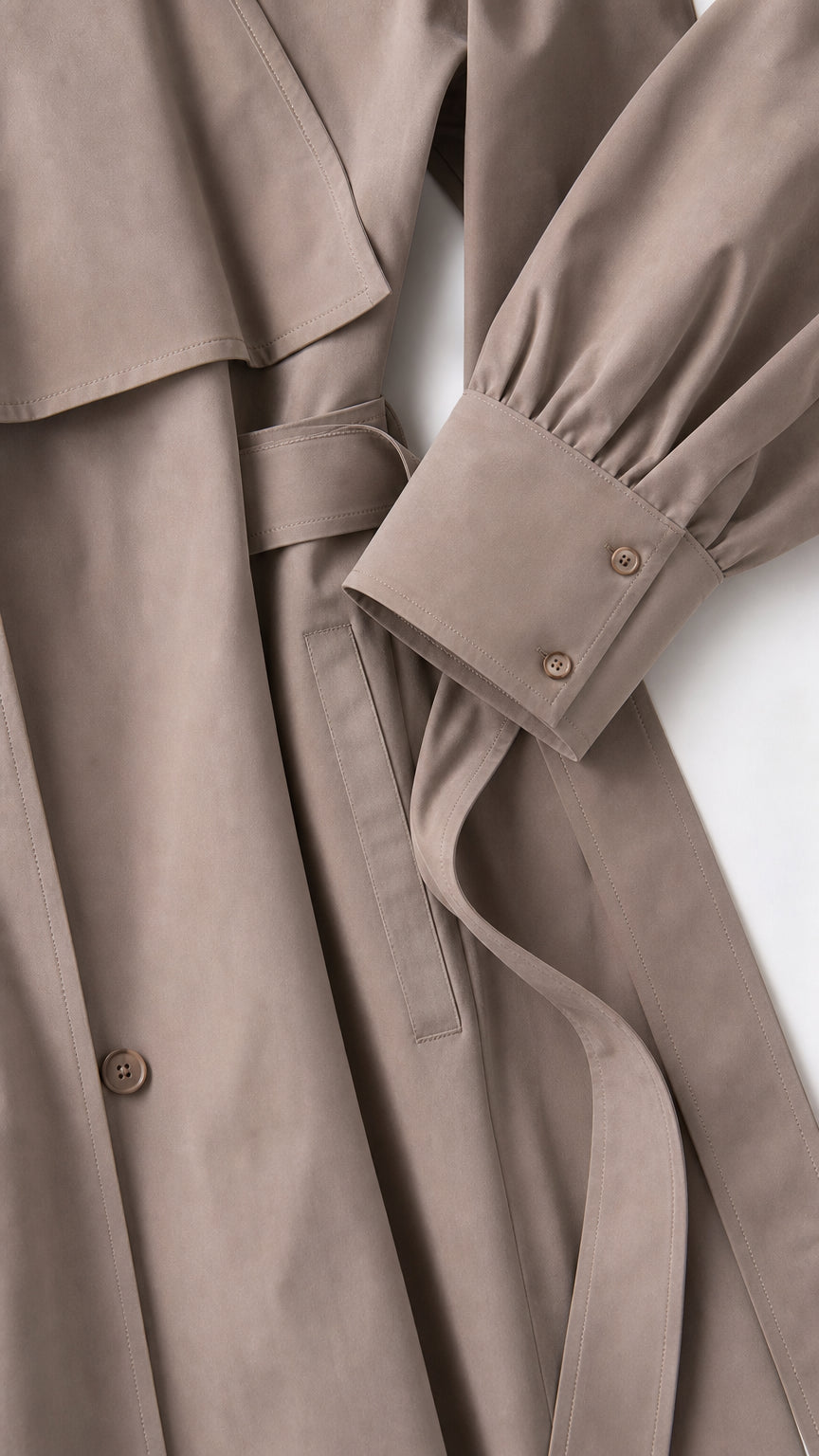 Close-up detail of the taupe brown coat fabric, belted waist, and tailored double-button sleeve cuff