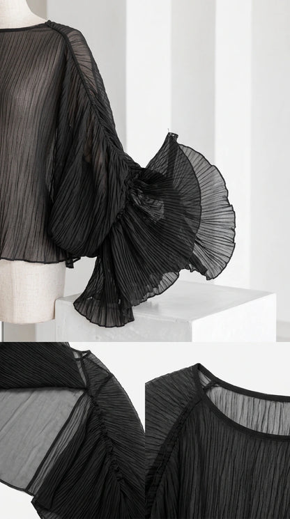 Close-up detail of sheer crinkled pleating, neckline, and flared bell sleeve construction in black