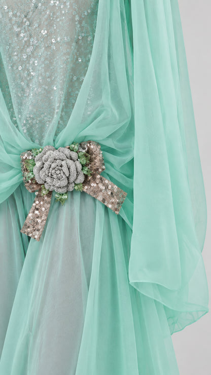 Close-up detail of sequined bodice, sheer draping, and beaded floral bow brooch