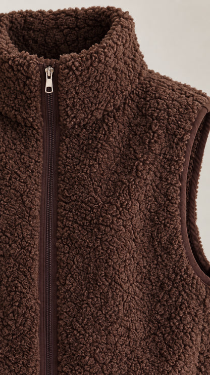 Close-up detail of brown sherpa fleece texture, zipper, and stand collar