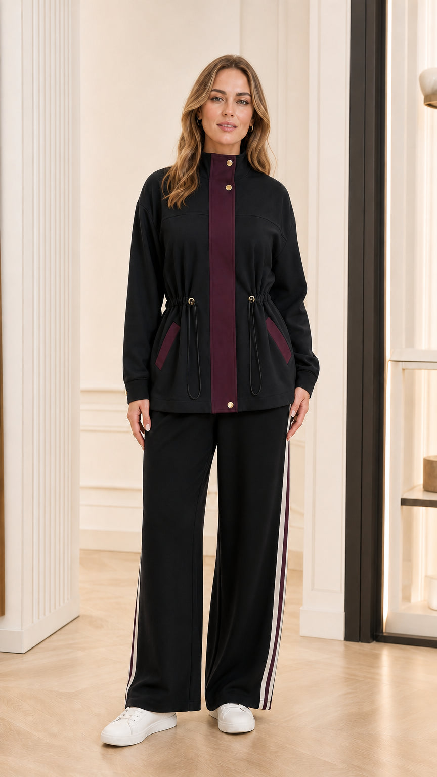 Model wearing black tracksuit jacket with burgundy placket and matching black wide-leg pants
