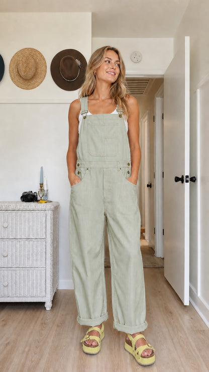 Model wearing sage green wide-leg bib overalls with rolled cuffs and side pockets