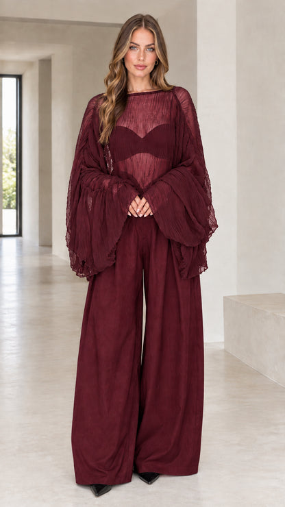 Front view of woman wearing burgundy sheer pleated bell sleeve top and wide-leg pants set