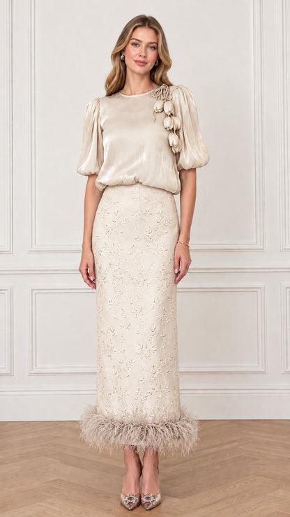 Model wearing Champagne gold puff sleeve top and embroidered column skirt with feather trim