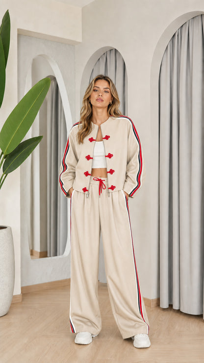 Model wearing beige two-piece tracksuit set with red accents