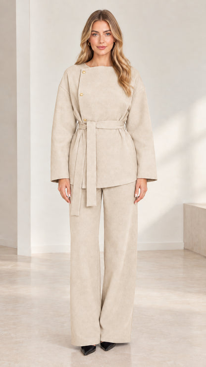 Full-length studio shot of model wearing beige cream asymmetrical belted pant set